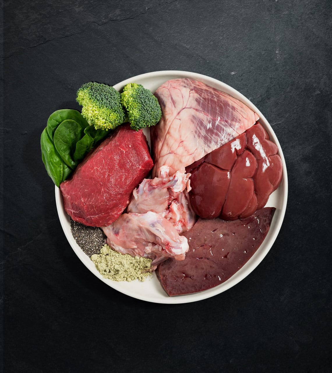 White bowl with Rawbone Mixed Protein Beef Meal, featuring raw beef, liver, heart, connective tissue, chia seeds, spinach, and supplements for species-appropriate nutrition.
