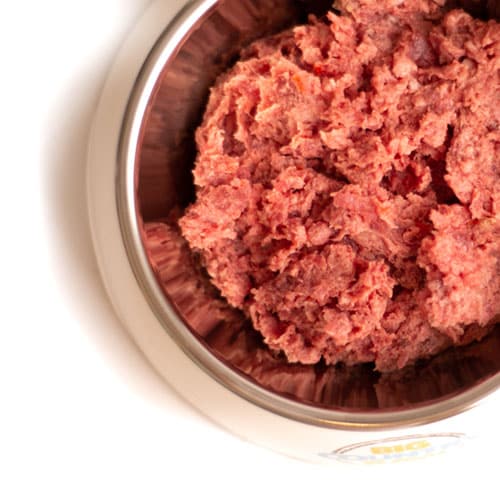 Stainless-steel bowl with finely ground pink meat, Big Country Raw Pork Dinner, packed with protein, hypoallergenic, ideal for active dogs with sensitivities.
