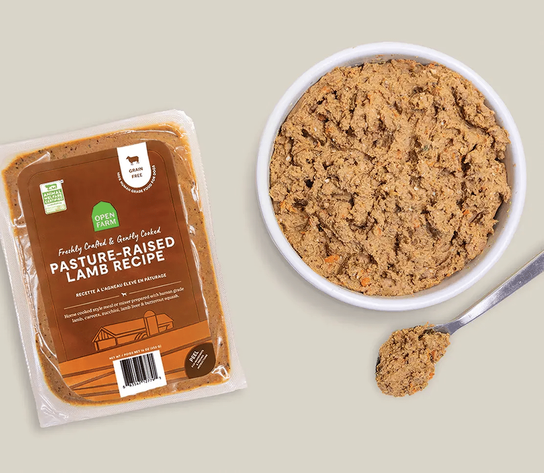 Open Farm Gently Cooked Pasture-Raised Lamb Recipe pouch beside a bowl with lamb-and-vegetable pâté, illustrating a human-grade, grain-free dog food option.