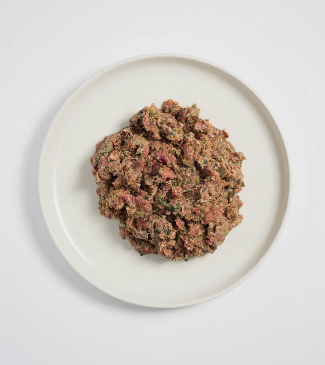 Rawbone Mixed Protein Lamb Meal on a white ceramic plate, featuring a raw minced meat blend with green flecks, ideal for canine nutrition.