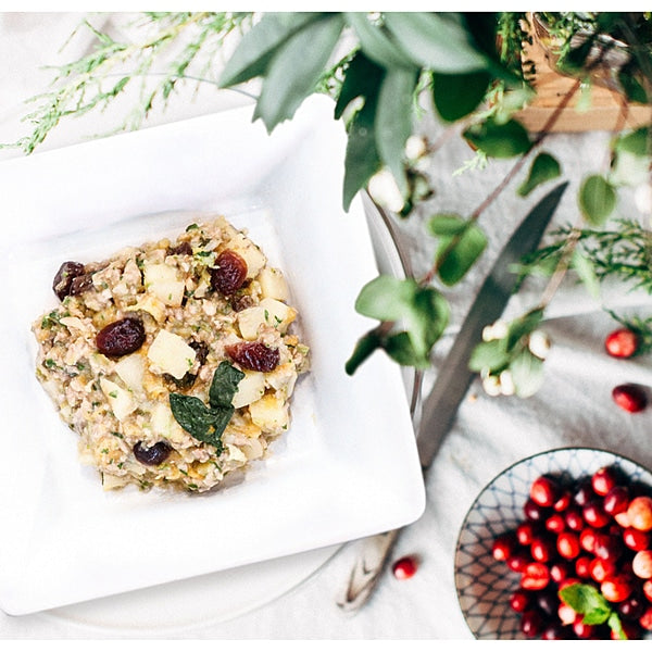 Tom & Sawyer Turkey Gobbler: A grain-based salad with cooked grains, diced green apple, dried cranberries, fresh herbs, and nuts on a white plate, with festive greenery.