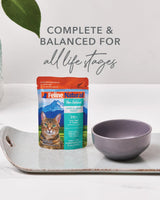 Feline Natural Pouches - Variety Box on tray with empty bowl; showcases New Zealand Hoki & Beef Feast, emphasizing complete nutrition for cats with protein-rich hydration.