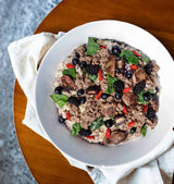 Tom & Sawyer Goji Berry Beef: a bowl of cooked grains topped with seasoned beef, fresh berries, greens, goji berries, and thin dark slices on a cloth napkin.