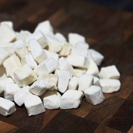 Cryogenically Freeze-Dried Calamari Bites 60g shown as small, white, soft cubes on a wooden board, ideal for cats and dogs, rich in nutrients.