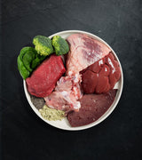 White bowl with Rawbone Mixed Protein Beef Meal, featuring raw beef, liver, heart, connective tissue, chia seeds, spinach, and supplements for species-appropriate nutrition.