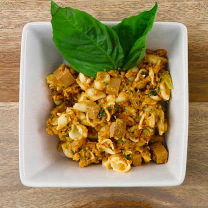 Tom & Sawyer Italian Beef Pasta in a white bowl, featuring shell pasta, green herb dressing, diced ingredients, and fresh basil leaves, on a wooden tabletop.