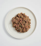 Rawbone Mixed Protein Lamb Meal on a white ceramic plate, featuring a raw minced meat blend with green flecks, ideal for canine nutrition.