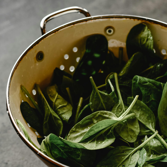 Spinach leaves in a metal colander on a dark surface