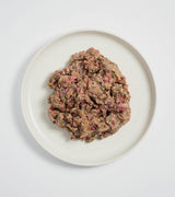 Rawbone Mixed Protein Chicken Meal on a white plate—coarsely minced, featuring chicken, herbs, and onion bits, highlighting a raw, freezer-friendly, species-appropriate meal.