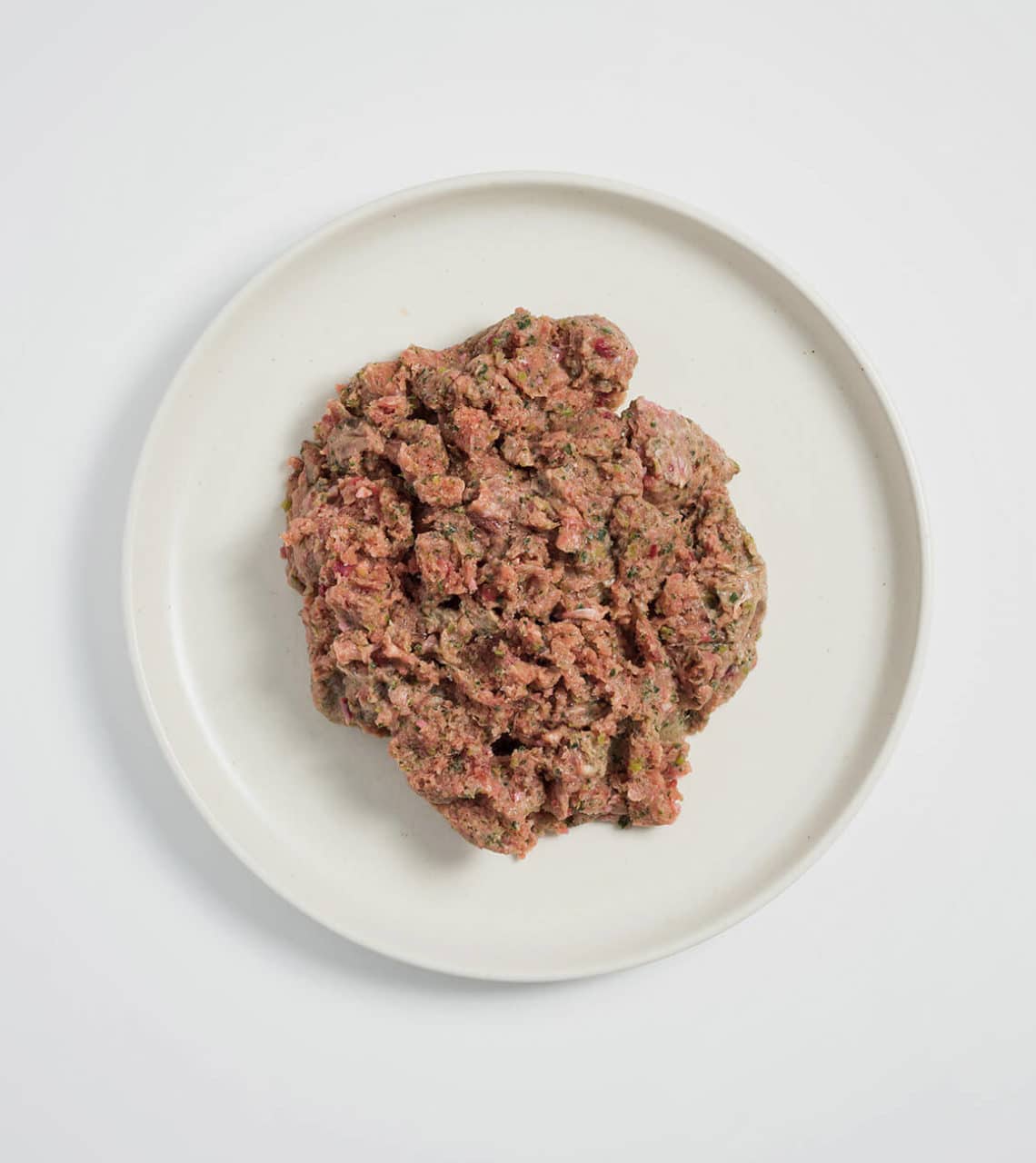 Rawbone Mixed Protein Pork Meal on a white plate, showcasing raw ground pork mixed with herbs and vegetables for a nutritious, ready-to-serve pet meal.